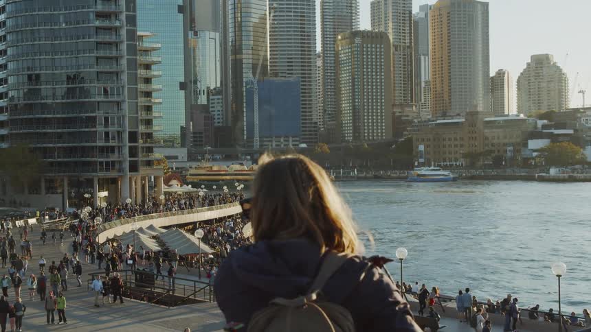 A woman is looking out over a busy harbor in a city during the day