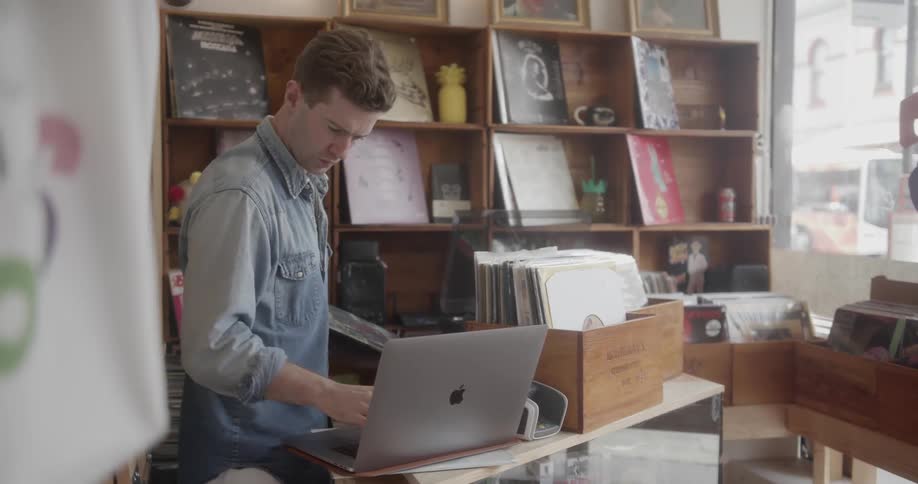 A man working in a record shop makes an entry on his laptop