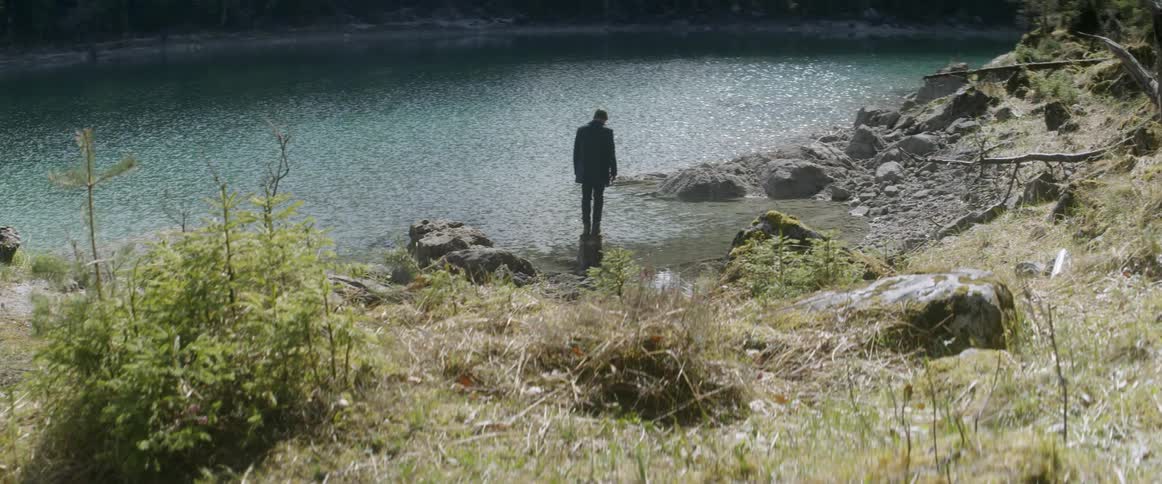 A man stands on a rock in shallow river water