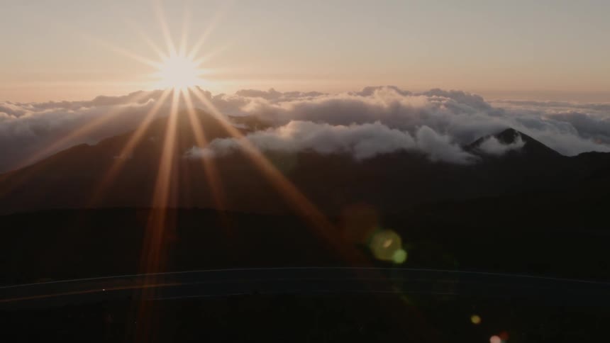 The sun shines brightly above the clouds and tall mountain