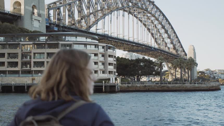A woman looks out over the water by the city bridge