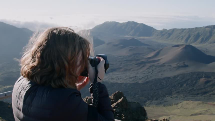 A woman takes pictures of the mountains from a high lookout