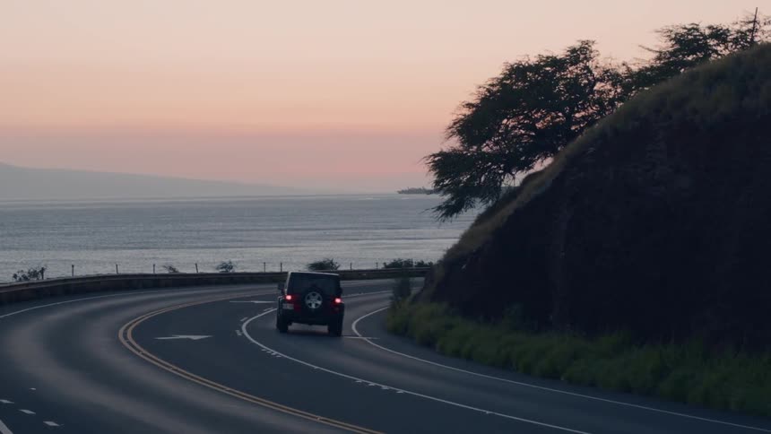 A red jeep travels down a coastline road