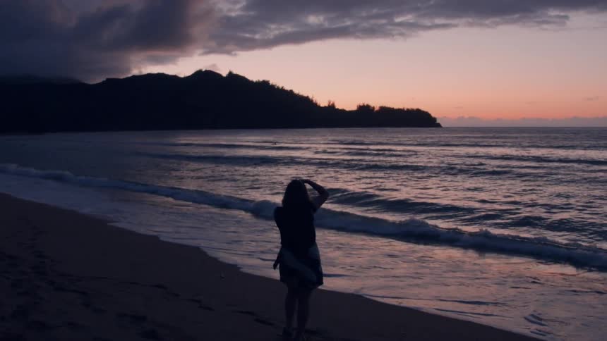 Woman taking photograph on ocean beach after sunset