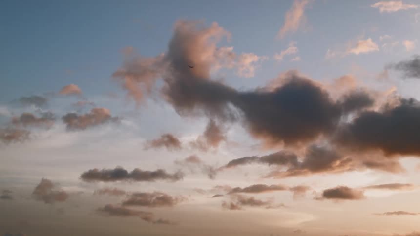 A plane flies below the clouds as the sun sets