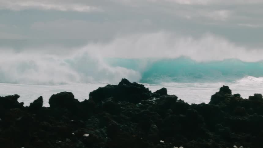 A wave is breaking and crashing toward the shore during the day