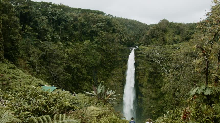 A waterfall is cascading over a cliff in a tropical setting during the day