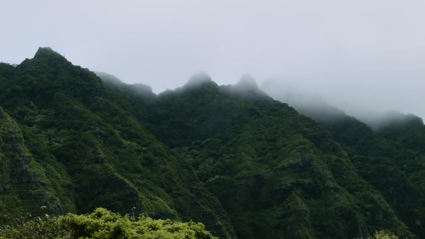 Clouds lingering near some green mountaintops