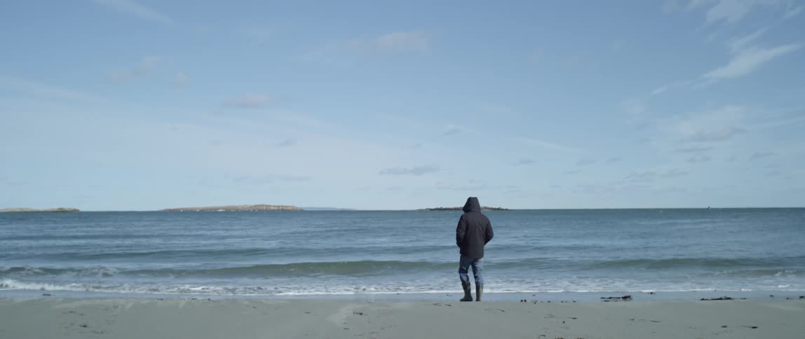 A man is walking toward the waves on a beach on a cold day