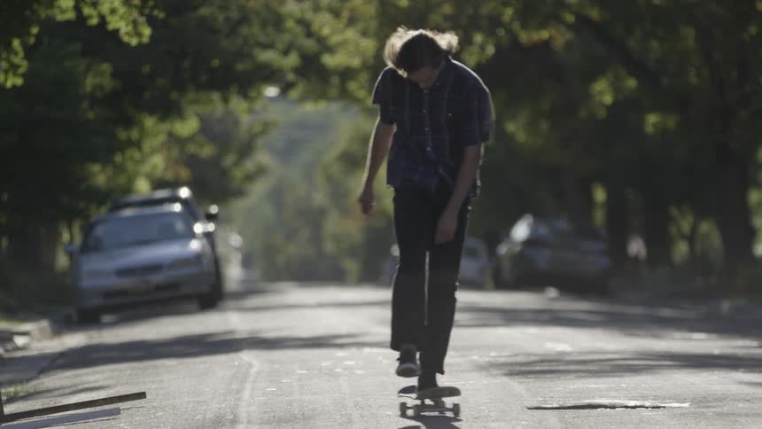 Man riding his skateboard up a street with trees on both sides