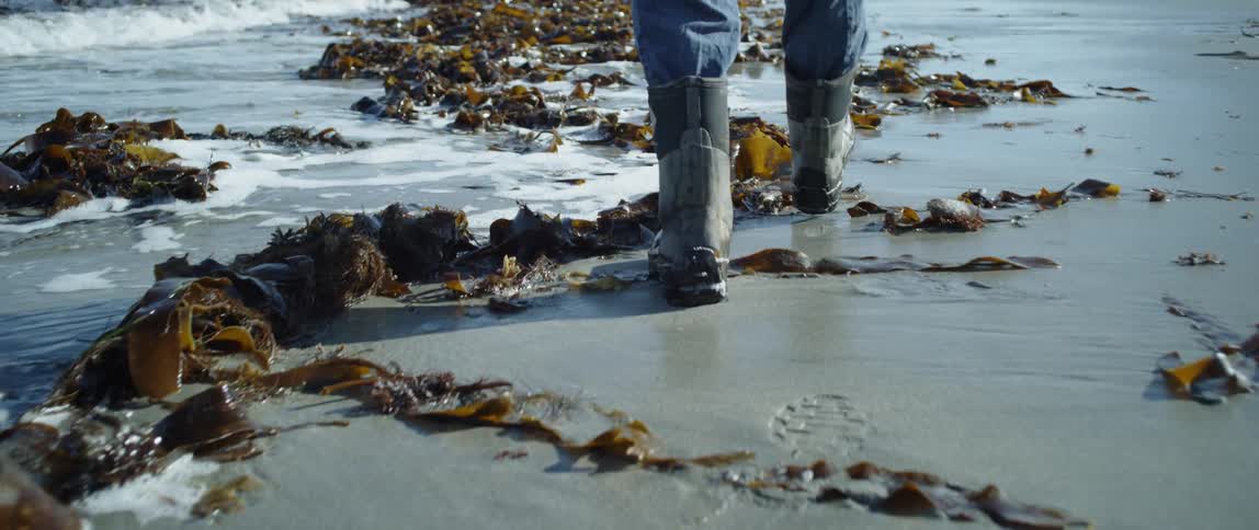 A man wades through wet sand in boots