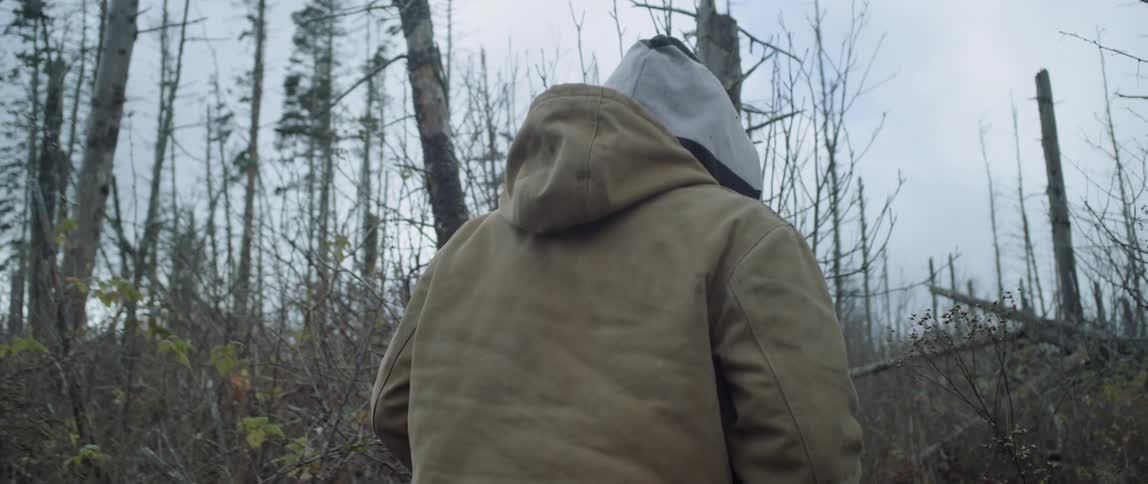 A man wearing a hoodie walks through the brush
