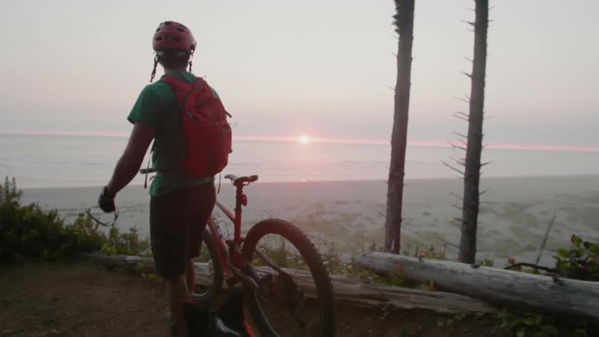 A man is walking his bike towards the shore on the hill