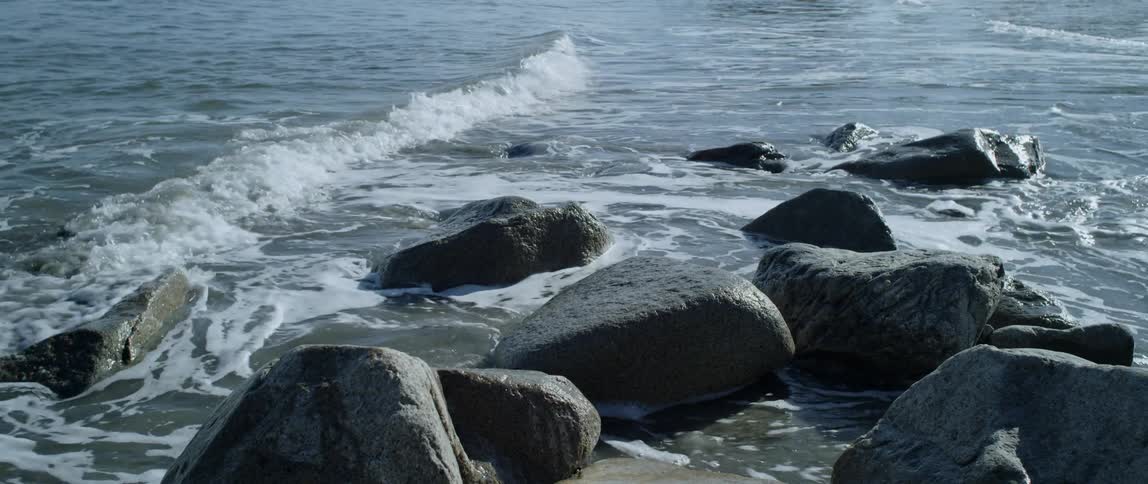 The tide flows onto the rocky covered shore