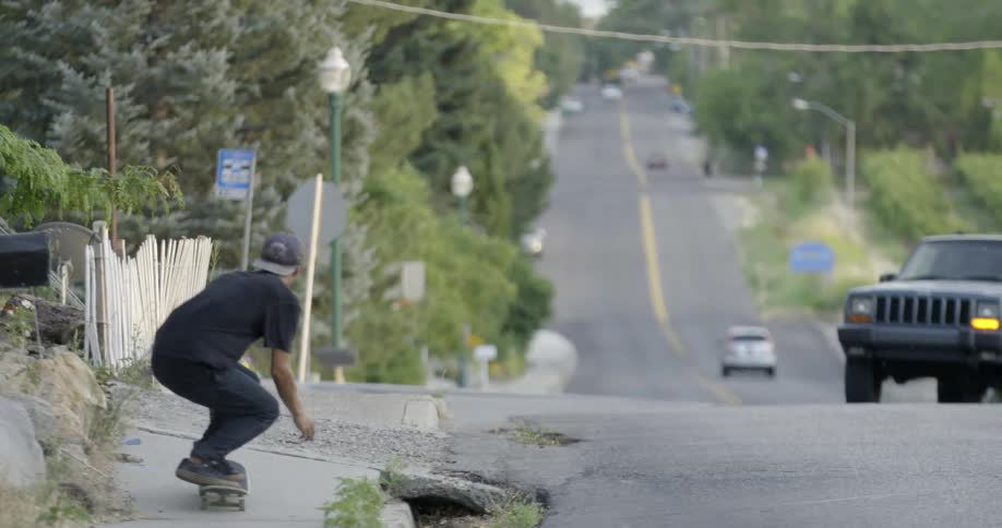 A young man skateboards and performs a jump down a city street as vehicles pass by