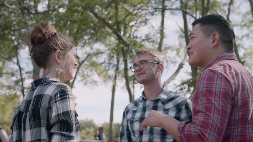 A woman is play hitting a man while standing outside in a park with him and a friend