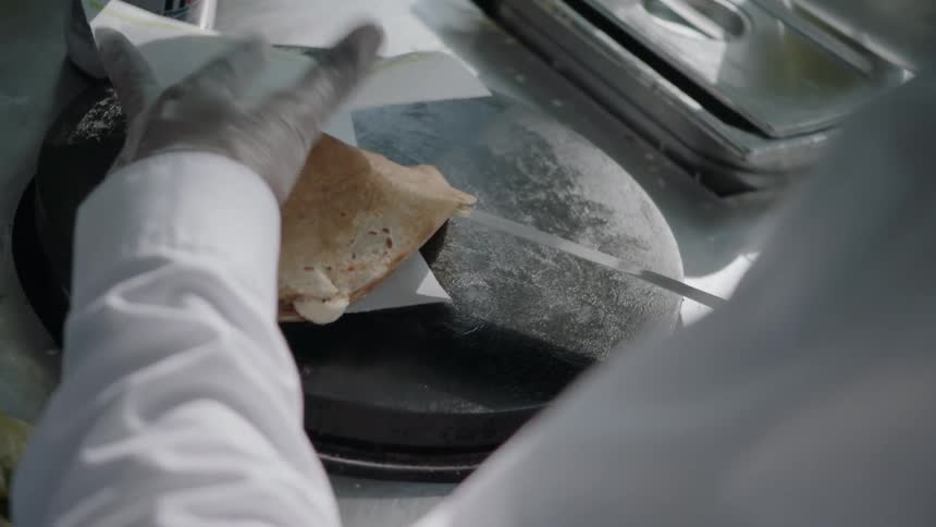 Someone is making a crepe and handing it to a customer