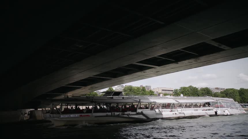 A ferry boat full of people travel under a bridge