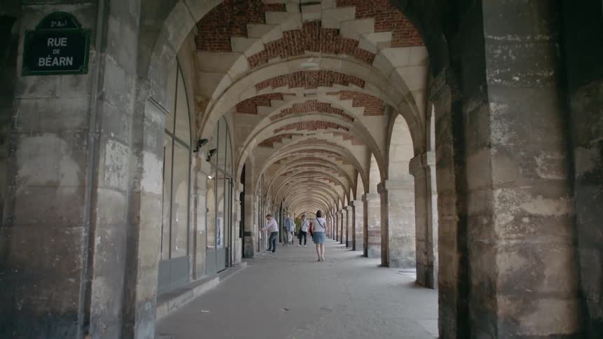 Tourists are walking beneath the arches of an old world building during the day