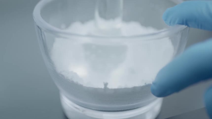 A scientist stirs white powder in a bowl