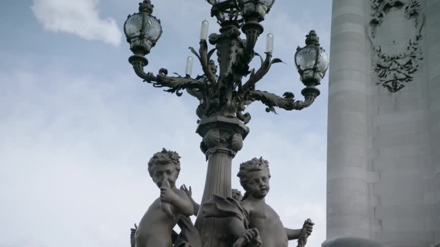 A large sculpture tower and ornate lamp post are displayed in the city