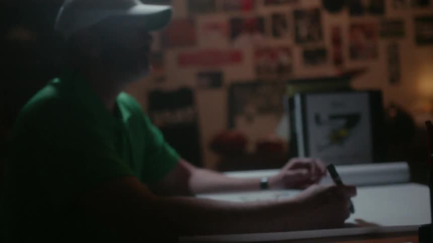 A man is opening a binder while sitting at a desk holding a pen