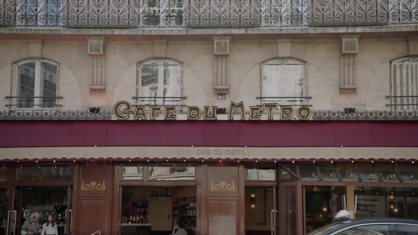 People leave a cafe as cars drive by