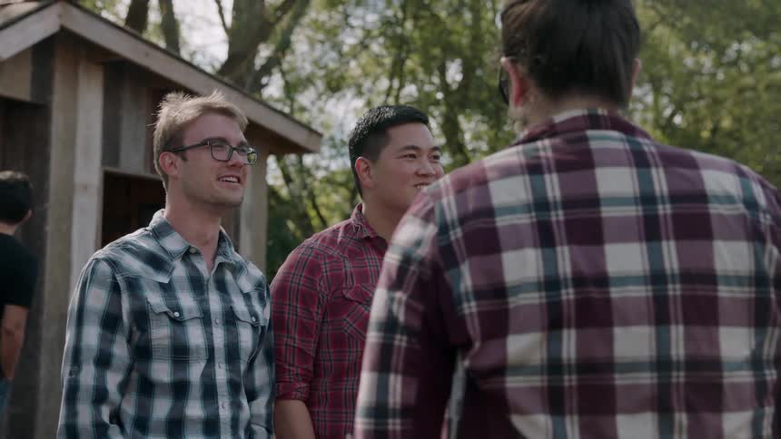 Two men and a woman are standing outside in a park talking during the day