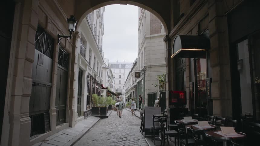 Tables and chairs are set up under an arch covered alleyway