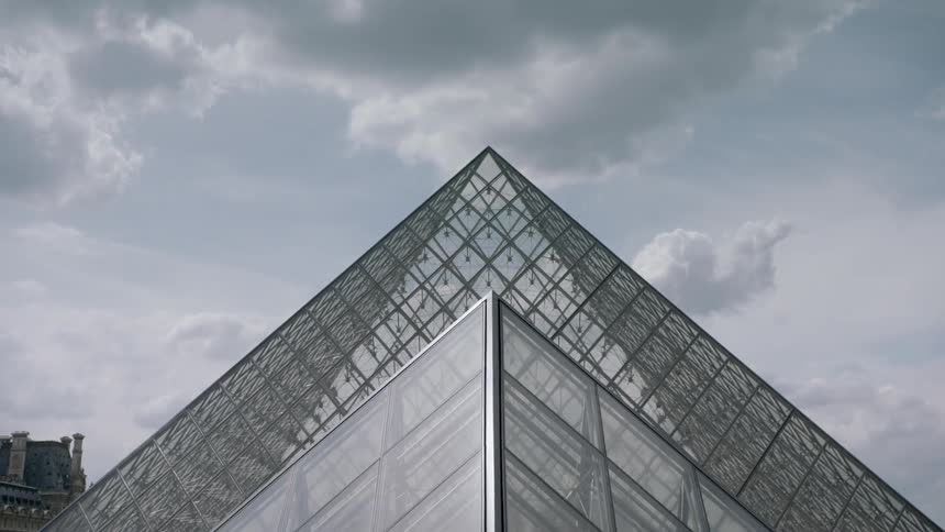 Clouds are hanging in the sky above the pyramid at the louvre during the day