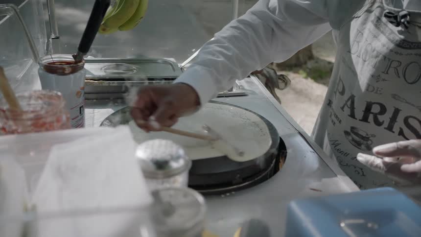 A person spreads crepe batter out onto a cooking stone
