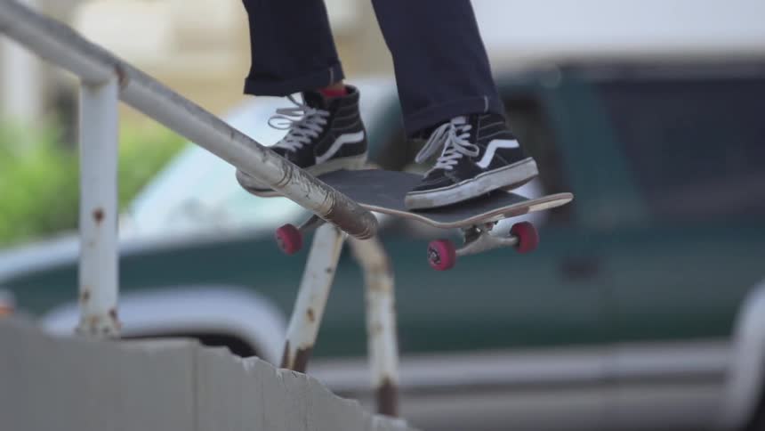 Person riding skateboard jumps on a railing as a car bases behind
