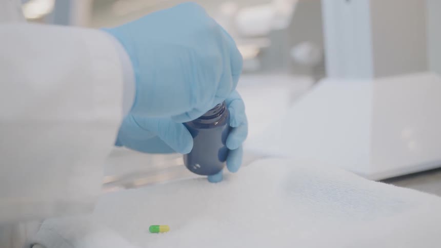 A worker wearing gloves places capsules in a bottle