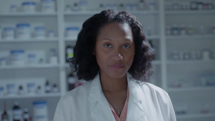 Woman wearing a lab coat stands near shelves of bottles