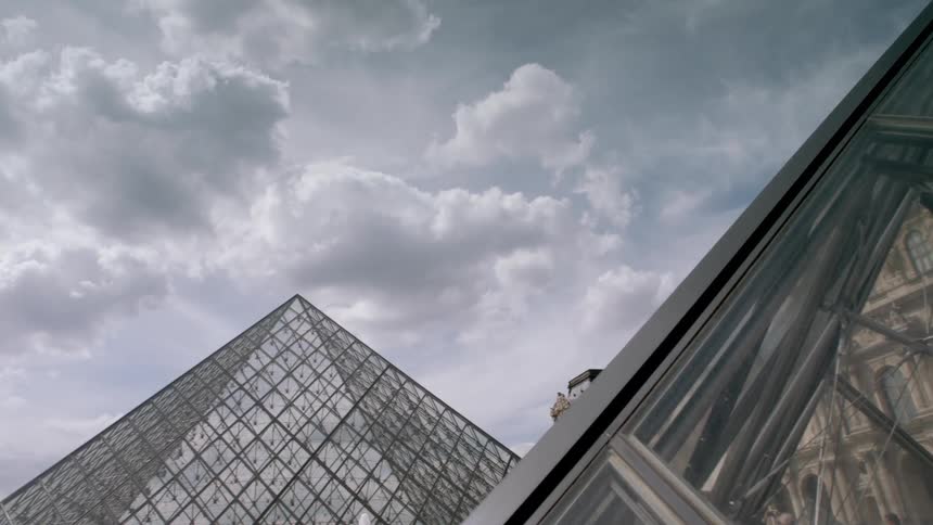 Pointed glass buildings surrounded by stone buildings on a cloudy day
