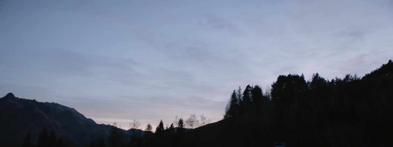 Clouds float above a mountain forest at sunset