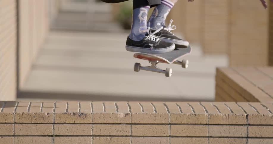 Man approaches, jumps and lands a skateboard trick over wall