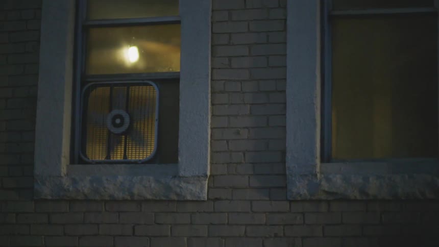 A fan is operating in a window of a building at dusk