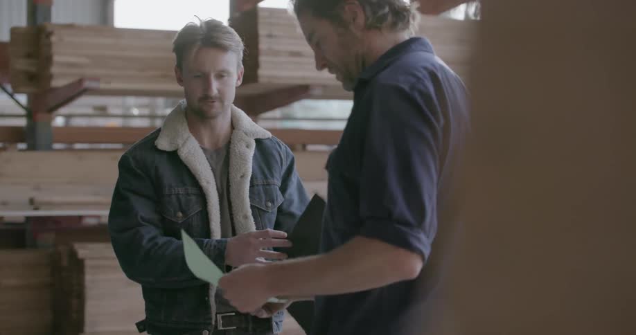 Two men exchange a handshake in a lumber warehouse