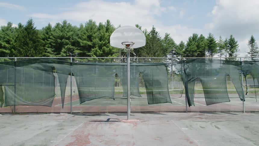 Tattered screening is blowing in the wind as it hangs from a basketball court fence