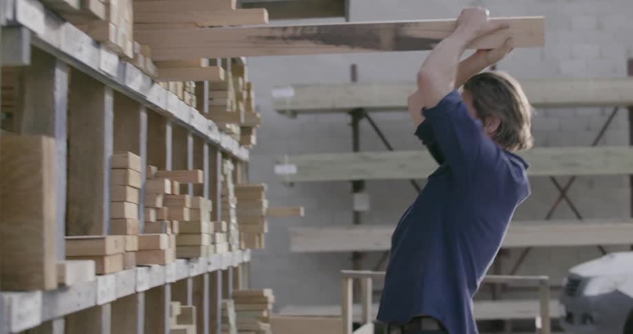 Man takes long piece of wood off a shelf outside