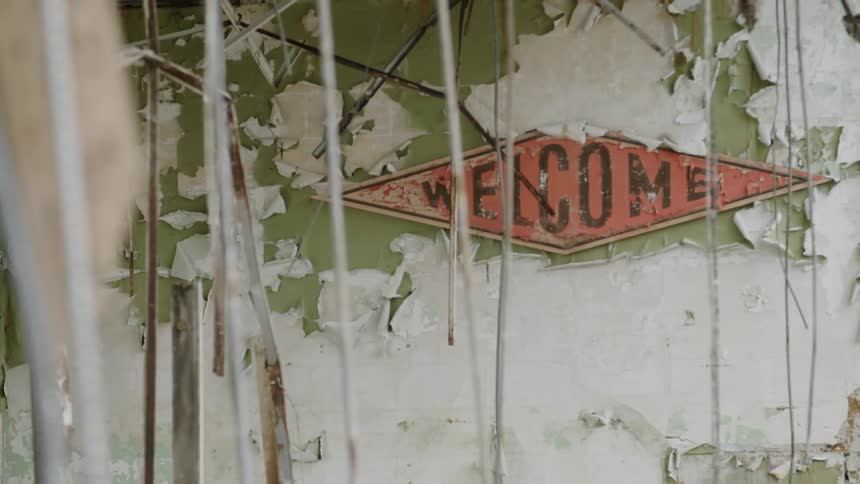 A welcome sign hangs on a dilapidated building
