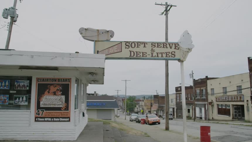 A dilapidated store sign stands outside a building in a small town during the day