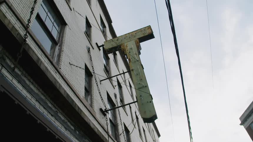 Old sign in the shape of the letter t fastened to a building in a city