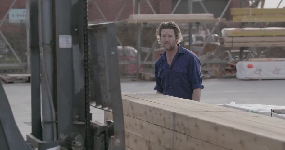 A man is instructing a forklift driver to lift some large pieces of wood and directing where to put it