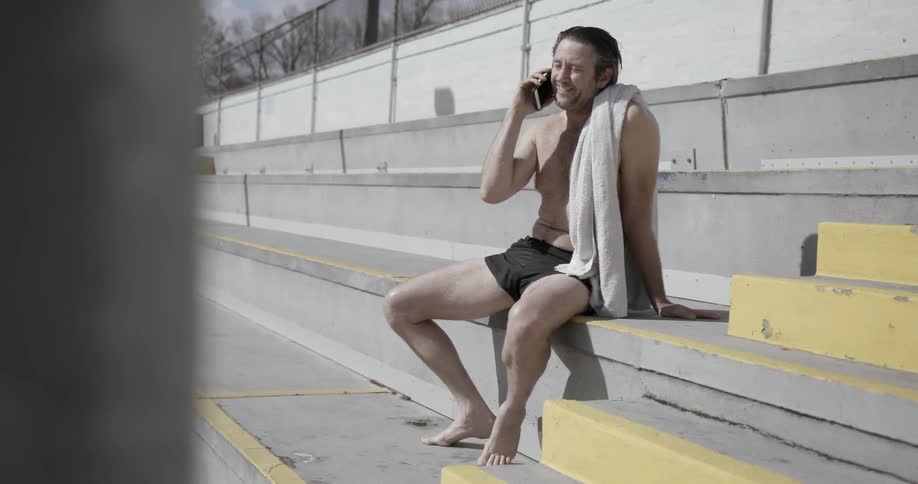 A man sits shirtless on bleachers talking on the cell phone