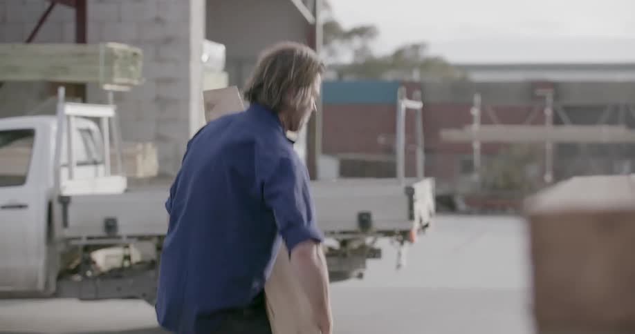 A man is picking up a wood board and carrying it toward a truck