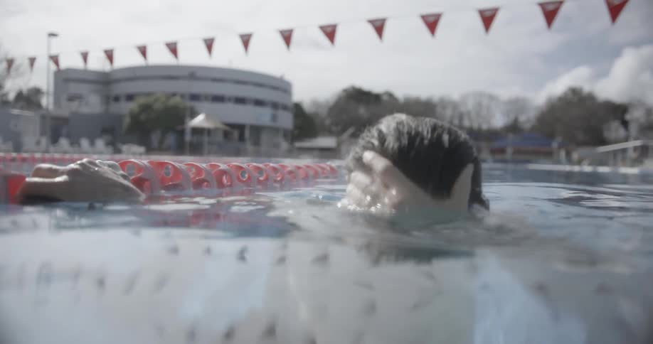Man pausing in the middle of a pool and wiping his hair back on a cloudy day