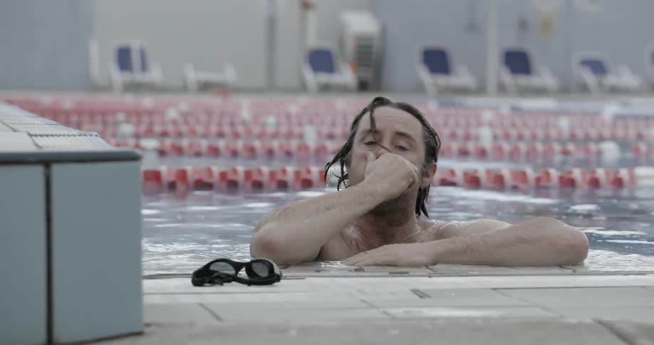 A man is coming up for air and taking off his goggles after going for a swim