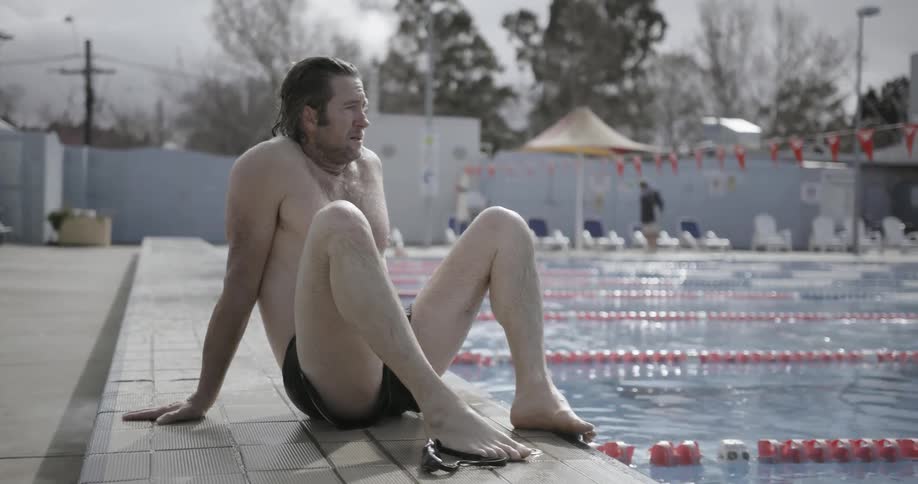 A man is sitting at the side of a pool and looking around during the day